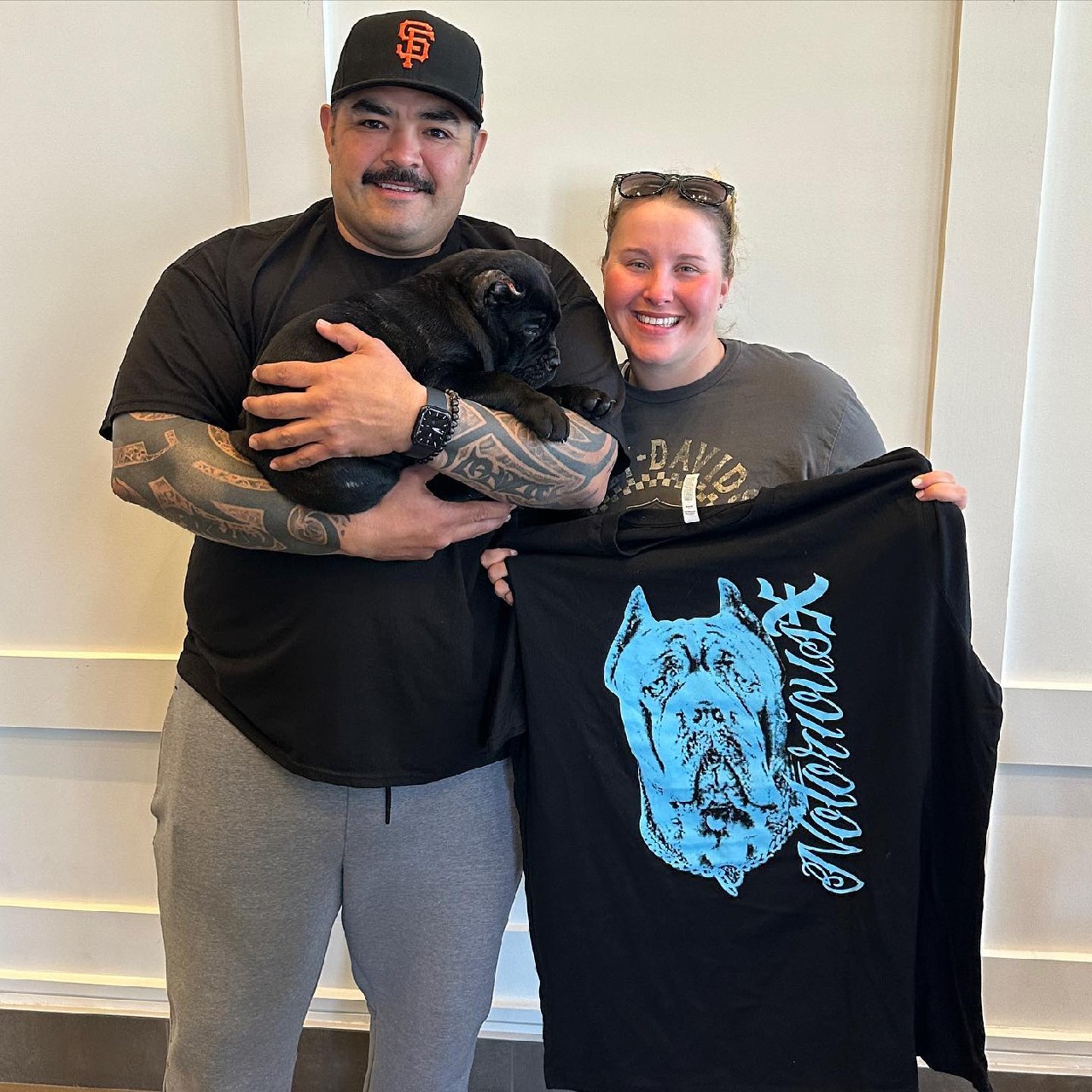 A couple in Nashville holding their black Cane Corso puppy and a Notorious X shirt on collection day